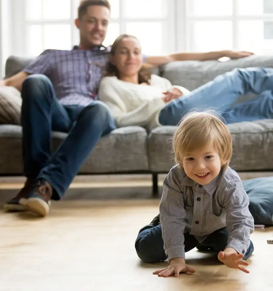 Own Homes image of mother and father sitting on sofa watching child crawling and playing on the floor
