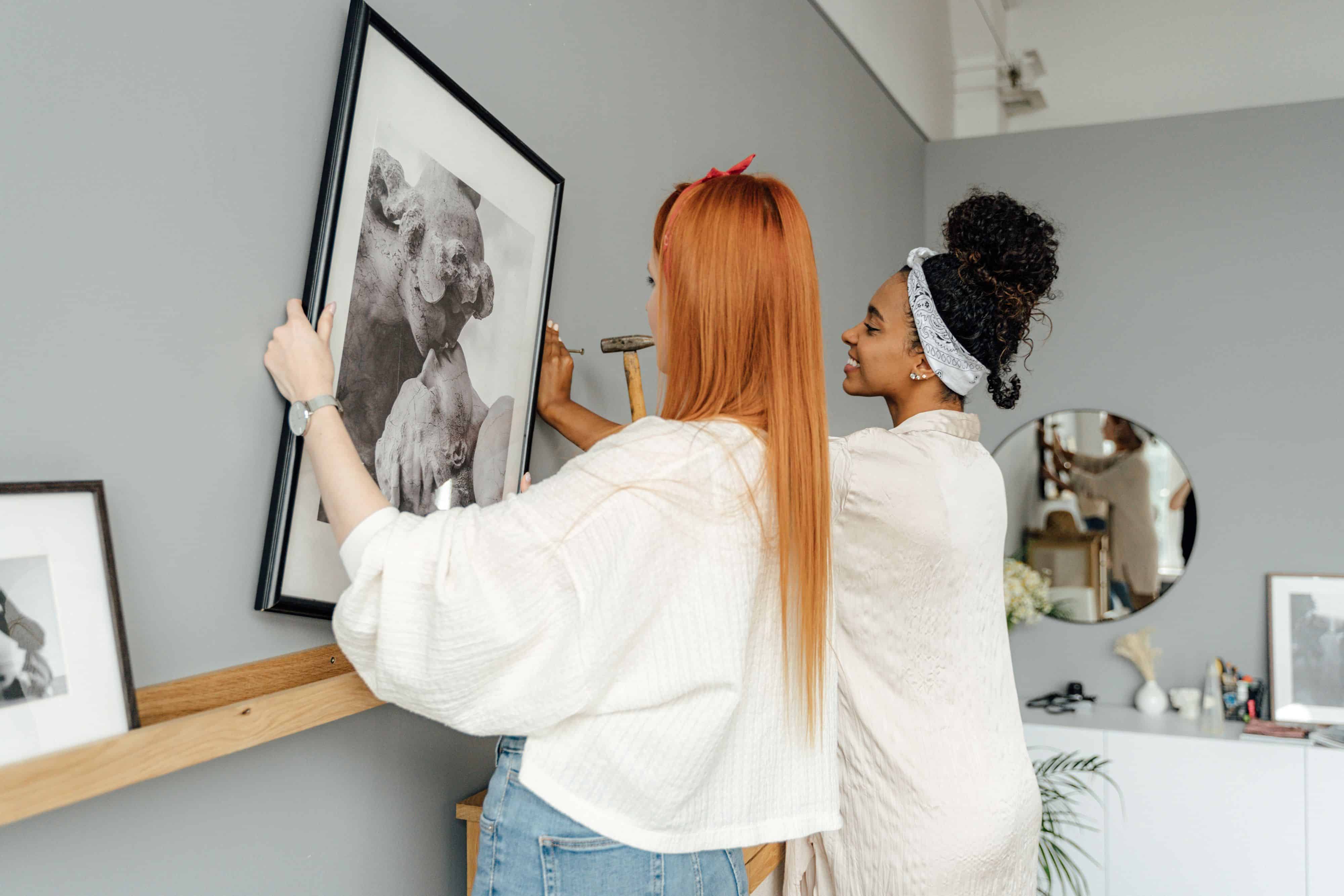 Two women hanging picture sin a new home | Own Homes